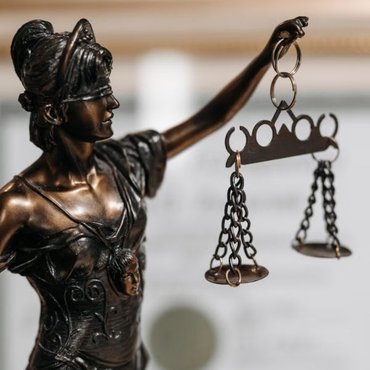 Bronze statue of Lady Justice holding scales, with a framed legal document in the background