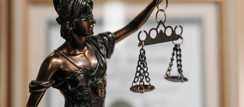 Bronze statue of Lady Justice holding scales, with a framed legal document in the background