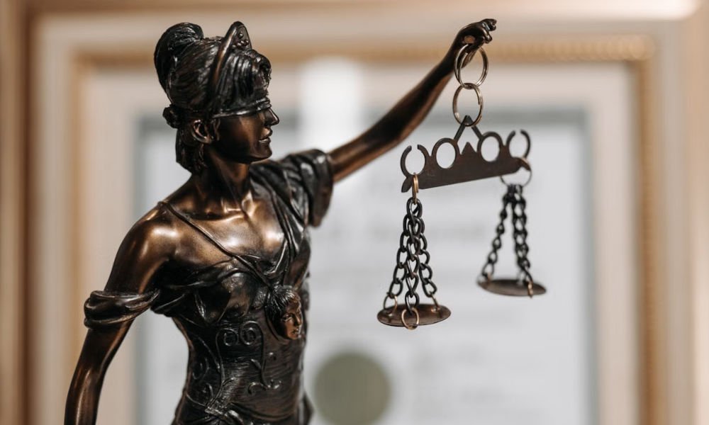 Bronze statue of Lady Justice holding scales, with a framed legal document in the background