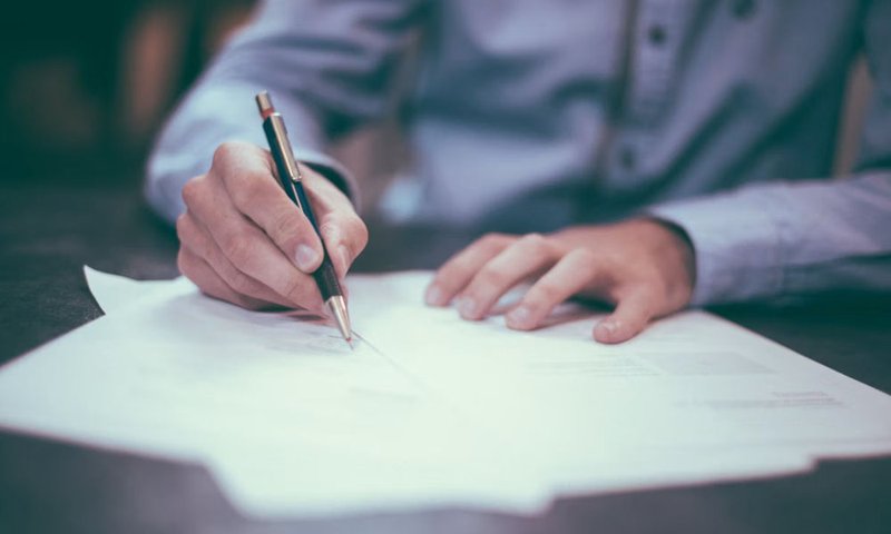 Person signing legal documents with a pen at a desk
