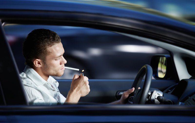 Driver lighting a cigarette inside a vehicle, illustrating situations where smoking may contribute to careless driving allegations under Ontario traffic law.