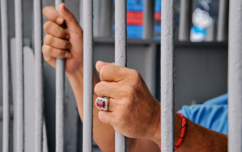 An individual behind prison bars represents the detention risks associated with breaching bail conditions in Canada