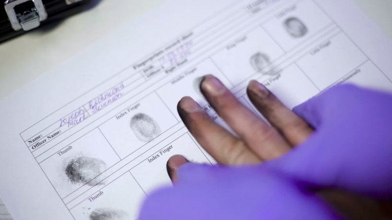 Police officer taking fingerprints as part of criminal record identification in Canada