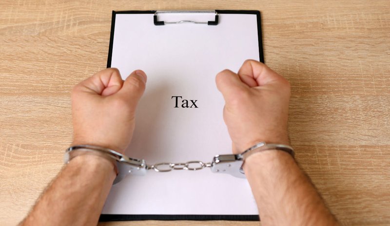 Man in handcuffs holding a document, symbolizing potential criminal prosecution and jail time for willful tax evasion in Canada.
