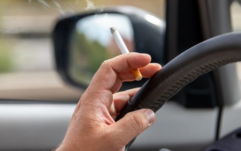 Close-up of a driver holding a cigarette while driving, illustrating how smoking may raise legal issues related to safe vehicle operation in Ontario.
